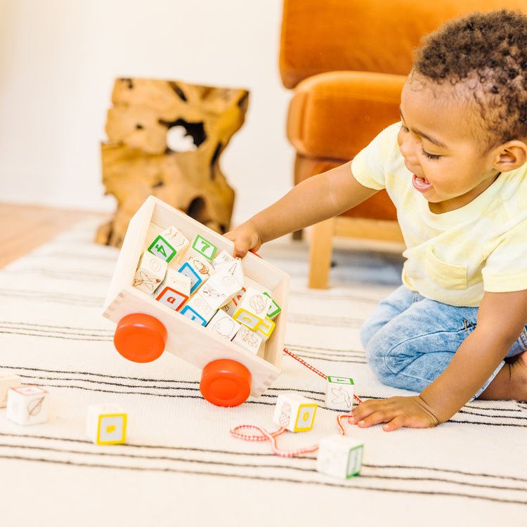 A kid playing with The Melissa & Doug Classic ABC Wooden Block Cart Educational Toy With 30 1-Inch Solid Wood Blocks