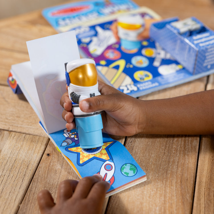 A kid playing with The Melissa & Doug Sticker WOW!™ Astronaut Bundle: 24-Page Activity Pad, Sticker Stamper, Mini Activity Pad, 500 Stickers, Arts and Crafts Fidget Toy Collectible Character