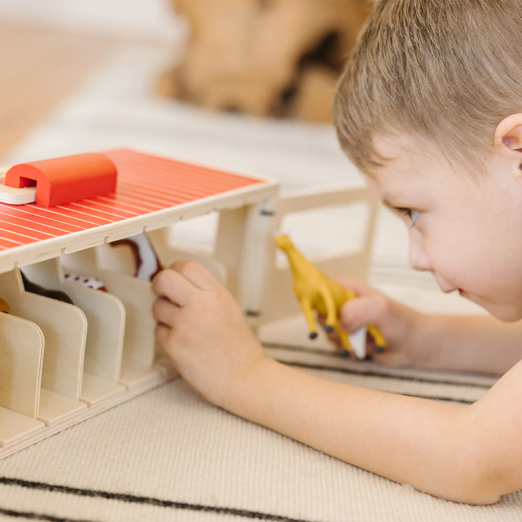 A kid playing with The Melissa & Doug Take-Along Show-Horse Stable Play Set With Wooden Stable Box and 8 Toy Horses