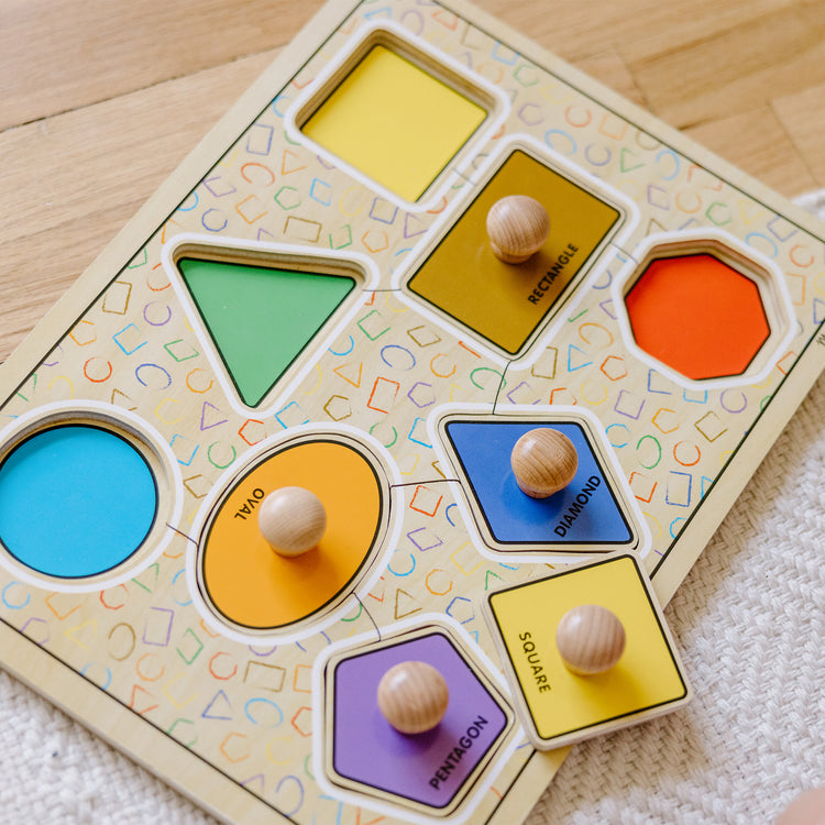 A kid playing with The Melissa & Doug Deluxe Jumbo Knob Wooden Puzzle - Geometric Shapes (8 pcs)