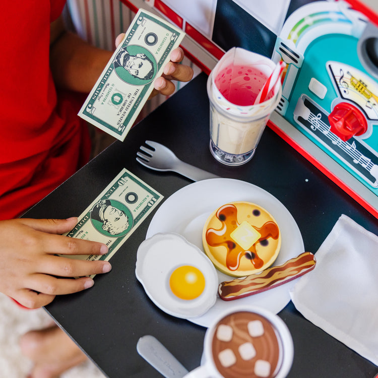 A kid playing with The Melissa & Doug Double-Sided Wooden Star Diner Restaurant Play Space