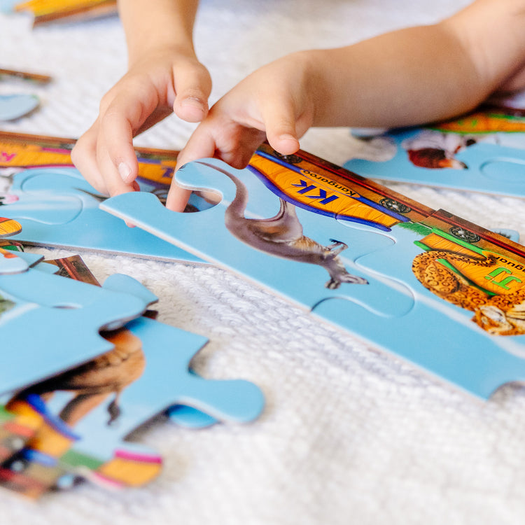 A kid playing with The Melissa & Doug Alphabet Train Jumbo Jigsaw Floor Puzzle - Letters and Animals (28 pcs, 10 feet long)