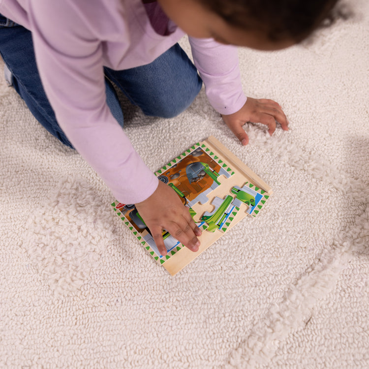 A kid playing with The Melissa & Doug Construction Vehicles 4-in-1 Wooden Jigsaw Puzzles in a Box (48 pcs)