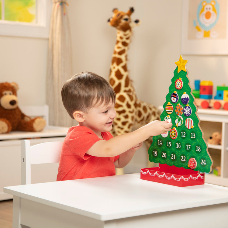 A kid playing with The Melissa & Doug Countdown to Christmas Wooden Advent Calendar - Magnetic Tree, 25 Magnets