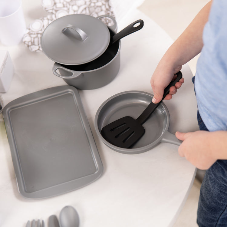 A kid playing with The Melissa & Doug 22-Piece Play Kitchen Accessories Set - Utensils, Pot, Pans, and More