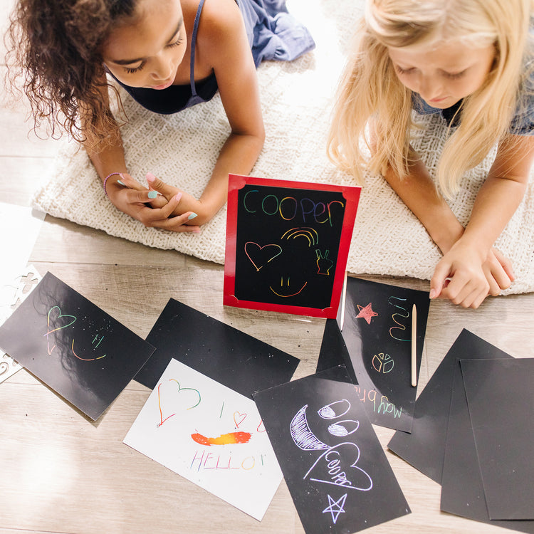 A kid playing with The Melissa & Doug Deluxe Combo Scratch Art Set: 16 Boards, 2 Stylus Tools, 3 Frames