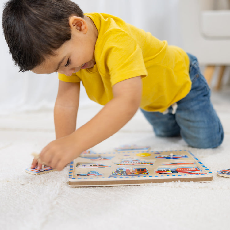 A kid playing with The Melissa & Doug Vehicles Sound Puzzle - Wooden Peg Puzzle With Sound Effects (8 pcs)