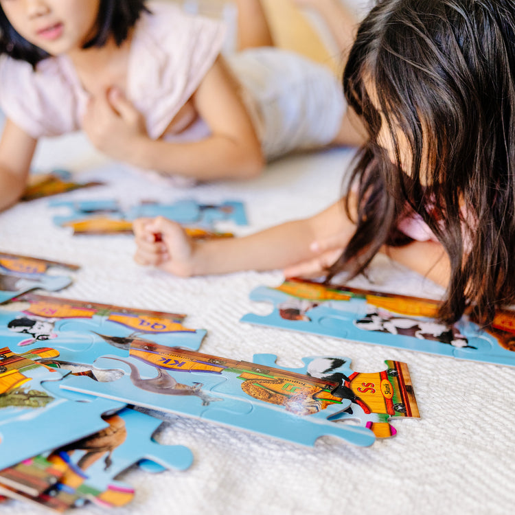 A kid playing with The Melissa & Doug Alphabet Train Jumbo Jigsaw Floor Puzzle - Letters and Animals (28 pcs, 10 feet long)