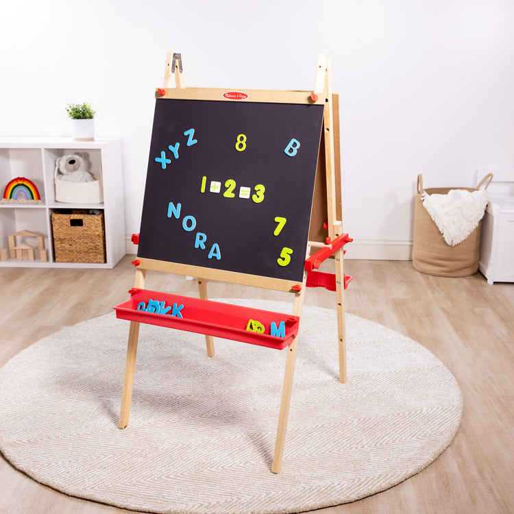 A playroom scene with The Melissa & Doug Deluxe Magnetic Standing Art Easel With Chalkboard, Dry-Erase Board, and 39 Letter and Number Magnets