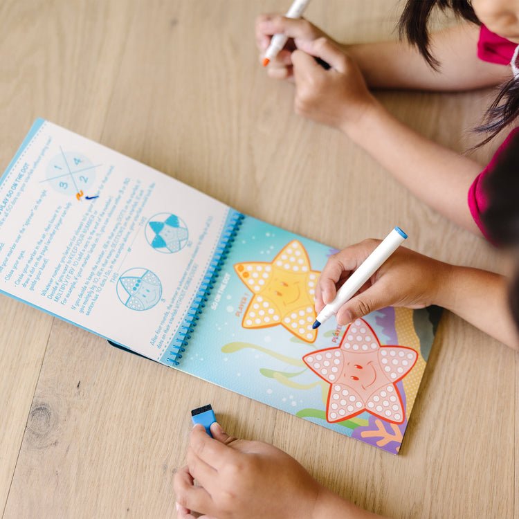 A kid playing with The Melissa & Doug On the Go Game On! Reusable Games Wipe-Off Activity Pad Reusable Travel Toy with 2 Dry-Erase Markers