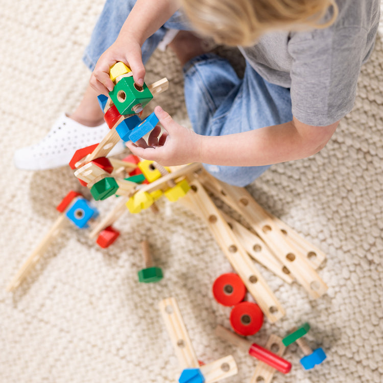 A kid playing with The Melissa & Doug Wooden Construction Building Toy Play Set in a Box, Developmental Educational Toy (48 pcs)