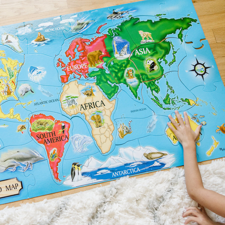 A kid playing with The Melissa & Doug World Map Jumbo Jigsaw Floor Puzzle (33 pcs, 2 x 3 feet)