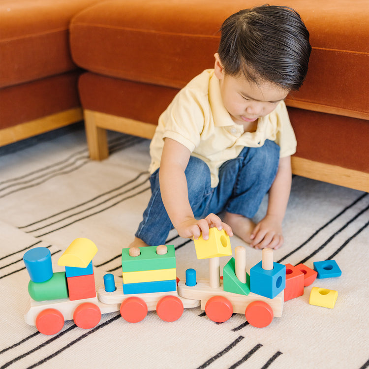 A kid playing with The Melissa & Doug Wooden Stacking Train Learning Toy Vehicle With 18 Connecting Pcs