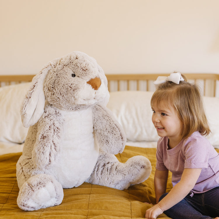 A kid playing with The Melissa & Doug Jumbo Burrow Bunny Lop-Eared Rabbit Stuffed Plush Animal (21 Inches Tall)