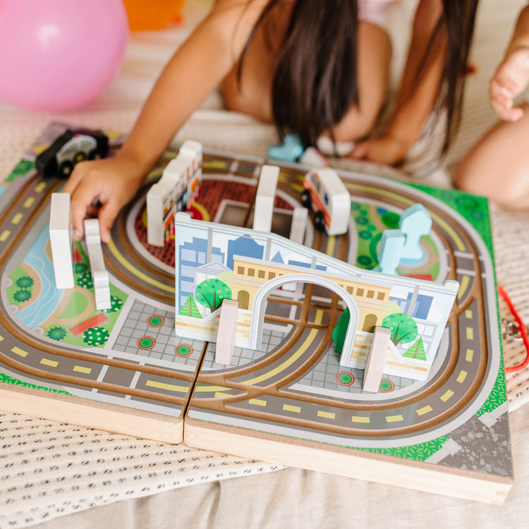 A kid playing with The Melissa & Doug 18-Piece Wooden Take-Along Tabletop Town, 4 Rescue Vehicles, Play Pieces, Bridge