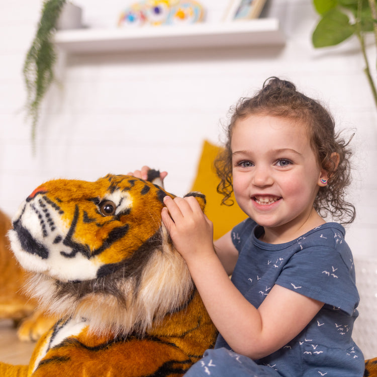 A kid playing with The Melissa & Doug Giant Tiger - Lifelike Stuffed Animal, Over 5 Feet Long (Includes Tail)