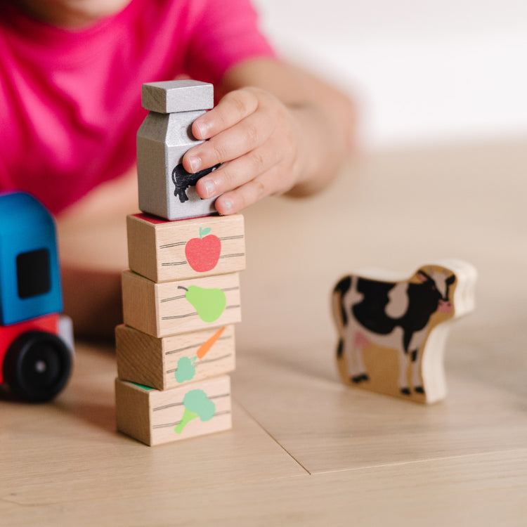 A kid playing with The Melissa & Doug Wooden Farm Train Set - Classic Wooden Toy (3 linking cars)