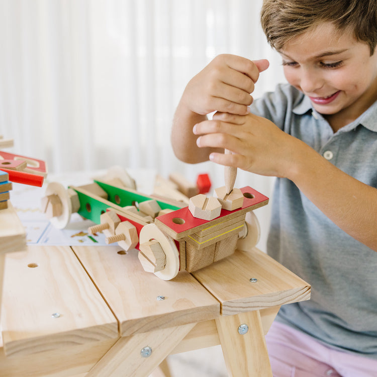 A kid playing with The Melissa & Doug Solid Wood Project Workbench Play Building Set