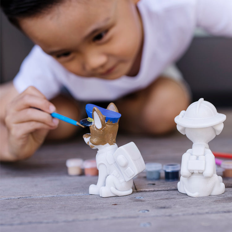 A kid playing with The Melissa & Doug PAW Patrol Craft Kit - 3 Decorate Your Own Pup Figurines