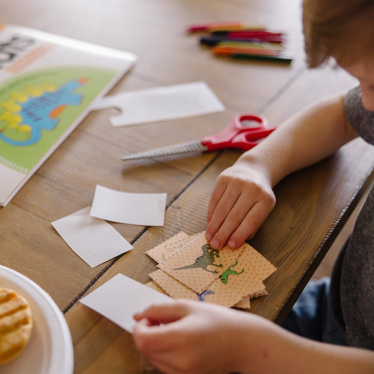 A kid playing with The Melissa & Doug Playmats Dinosaurs Take-Along Paper Coloring And Learning Activity Pads (24 Pages)