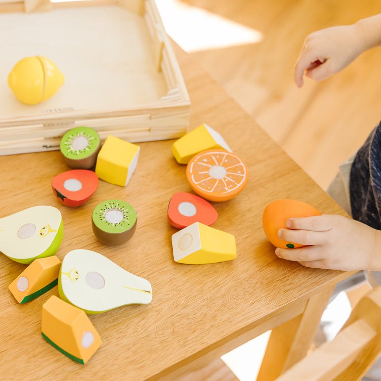 A kid playing with The Melissa & Doug Cutting Fruit Set - Wooden Play Food Kitchen Accessory, Multi