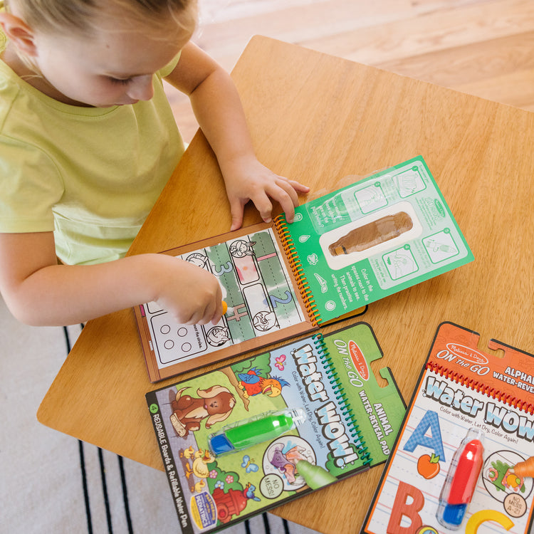 A kid playing with The Melissa & Doug Water Wow! - Water Reveal Pad Bundle - Animals, Alphabet, Numbers and More