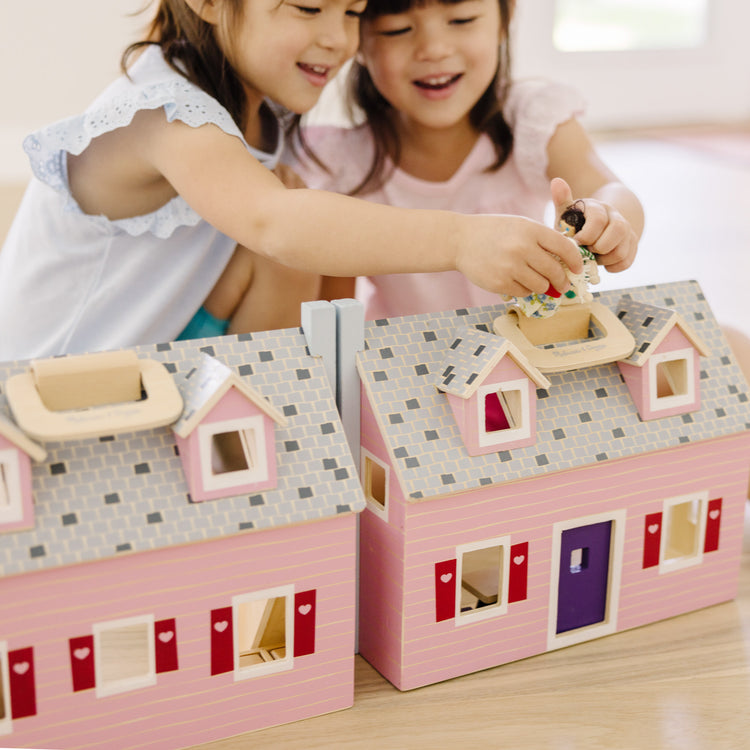 A kid playing with The Melissa & Doug Fold and Go Wooden Dollhouse With 2 Dolls and Wooden Furniture