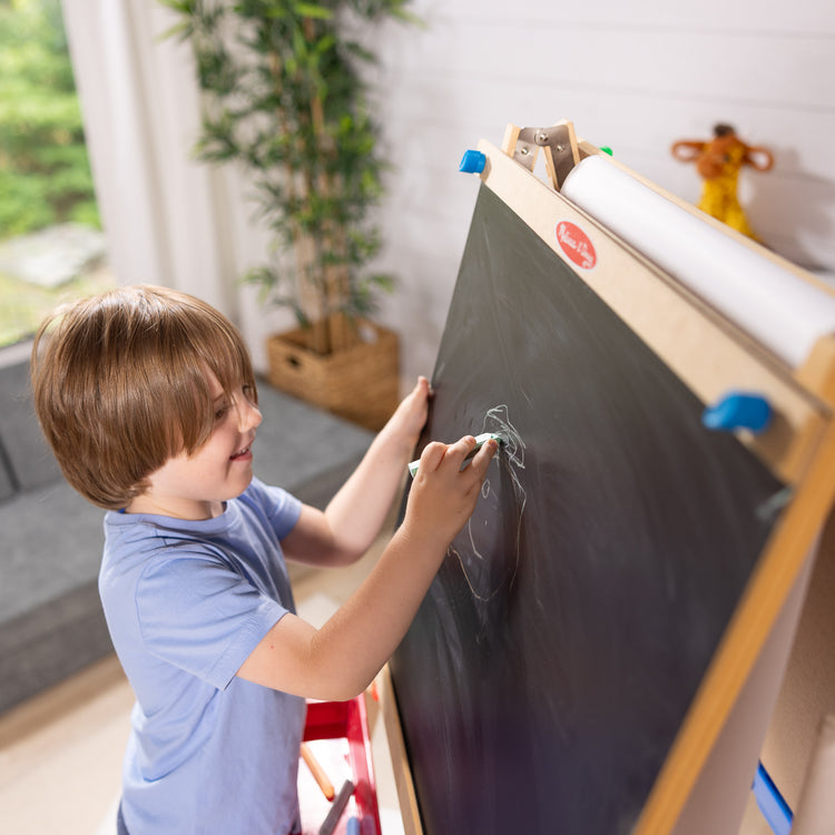 A kid playing with The Melissa & Doug Deluxe Standing Art Easel - Dry-Erase Board, Chalkboard, Paper Roller