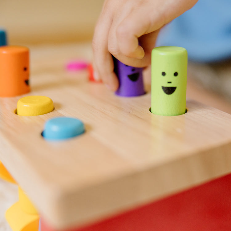 A kid playing with The Melissa & Doug Deluxe Pounding Bench Wooden Preschool Learning Toy With Mallet