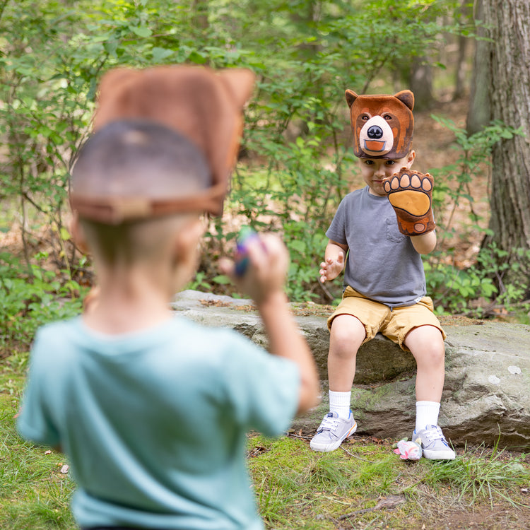 A kid playing with The Melissa & Doug Yellowstone National Park Grizzly Bear Games and Pretend Play Set with Plush Bear Heads and Bear Paw Gloves