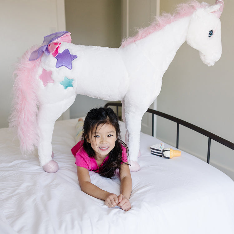 A kid playing with The Melissa & Doug Giant Unicorn - Lifelike Plush Stuffed Animal (over 2 feet tall)