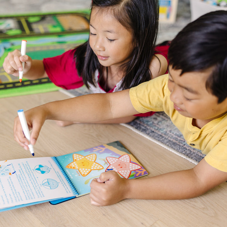 A kid playing with The Melissa & Doug On the Go Game On! Reusable Games Wipe-Off Activity Pad Reusable Travel Toy with 2 Dry-Erase Markers