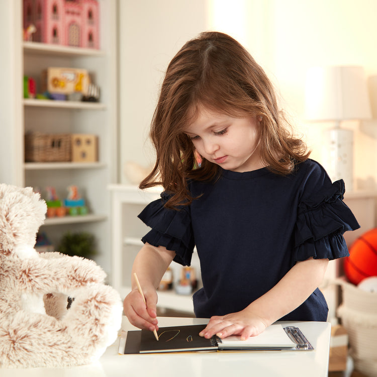 A kid playing with The Melissa & Doug Scratch Art Doodle Pad With 16 Scratch-Art Boards and Wooden Stylus