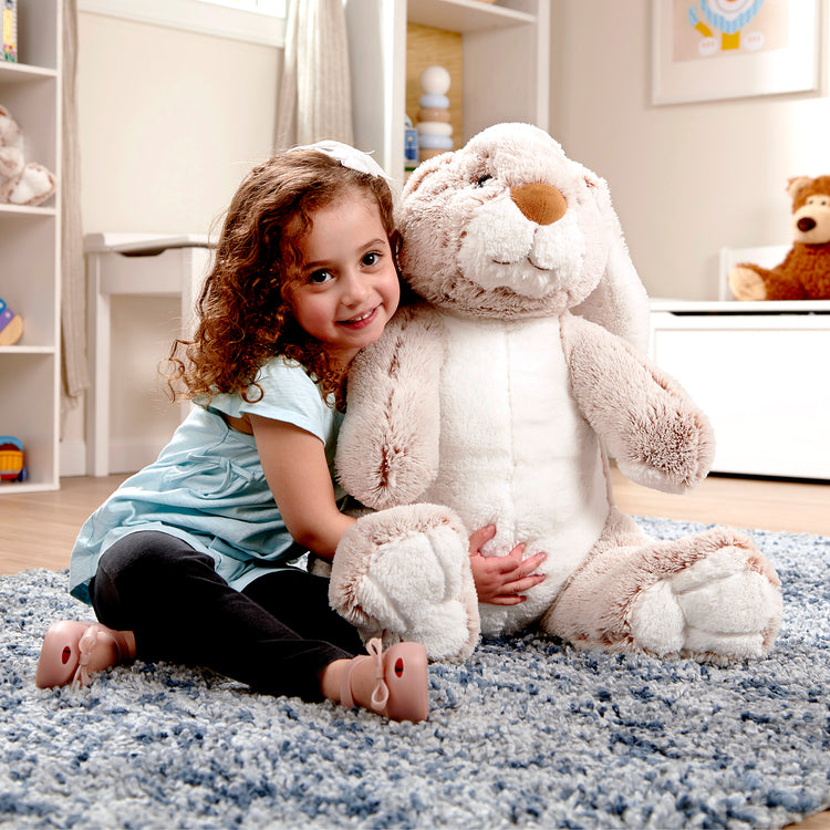 A kid playing with The Melissa & Doug Jumbo Burrow Bunny Lop-Eared Rabbit Stuffed Plush Animal (21 Inches Tall)