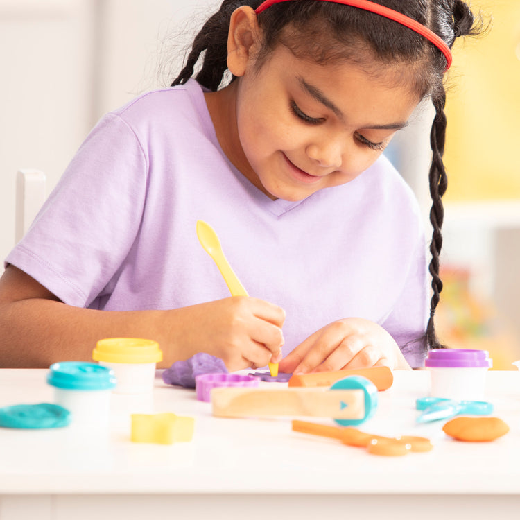 A kid playing with The Melissa & Doug Clay Play Activity Set - With Sculpting Tools and 8 Tubs of Modeling Dough