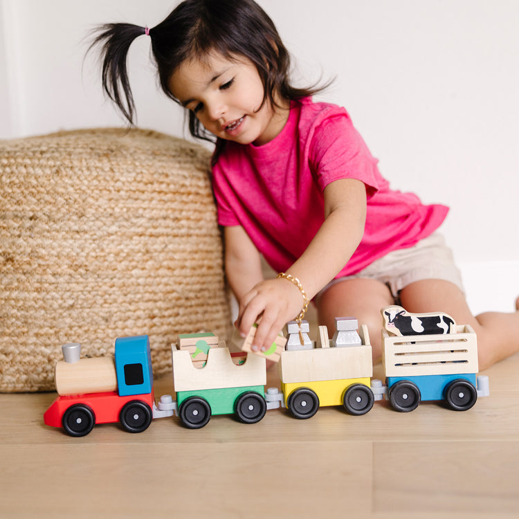 A kid playing with The Melissa & Doug Wooden Farm Train Set - Classic Wooden Toy (3 linking cars)