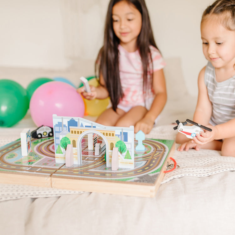 A kid playing with The Melissa & Doug 18-Piece Wooden Take-Along Tabletop Town, 4 Rescue Vehicles, Play Pieces, Bridge