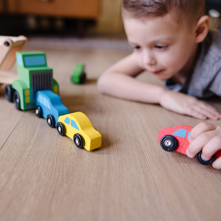 A kid playing with The Melissa & Doug Car Carrier Truck and Cars Wooden Toy Set With 1 Truck and 4 Cars