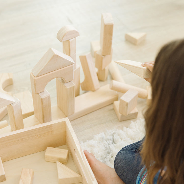 A kid playing with The Melissa & Doug Standard Unit Solid-Wood Building Blocks With Wooden Storage Tray (60 pcs)