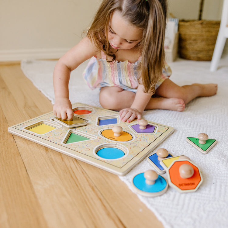 A kid playing with The Melissa & Doug Deluxe Jumbo Knob Wooden Puzzle - Geometric Shapes (8 pcs)