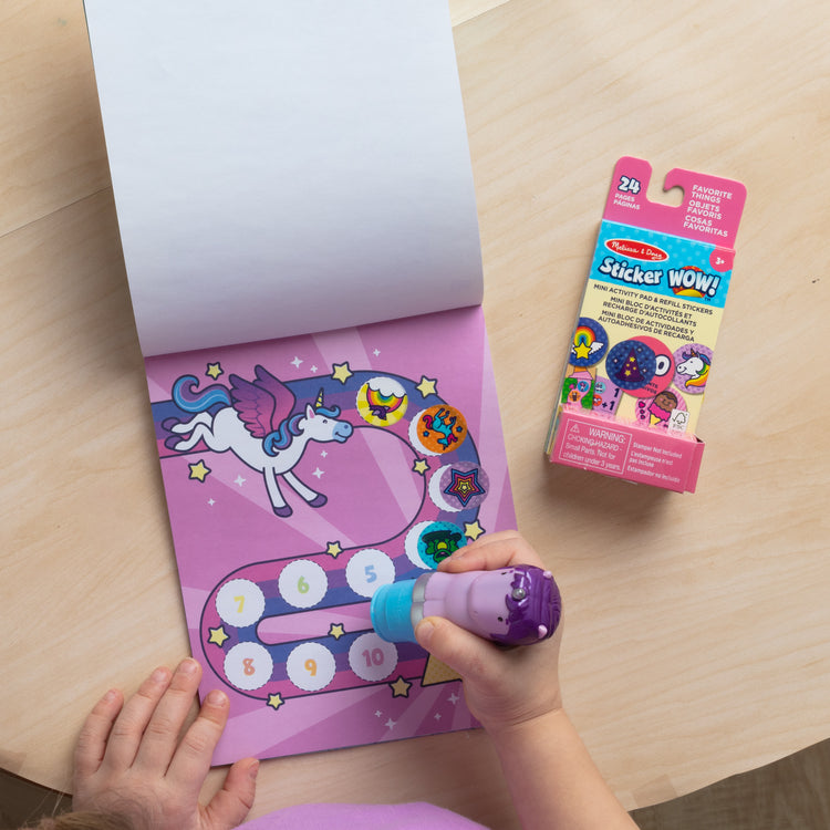 A kid playing with The Melissa & Doug Sticker WOW!™ Purple Unicorn Bundle: 24-Page Activity Pad, Sticker Stamper, 500 Stickers, Arts and Crafts Fidget Toy Collectible Character