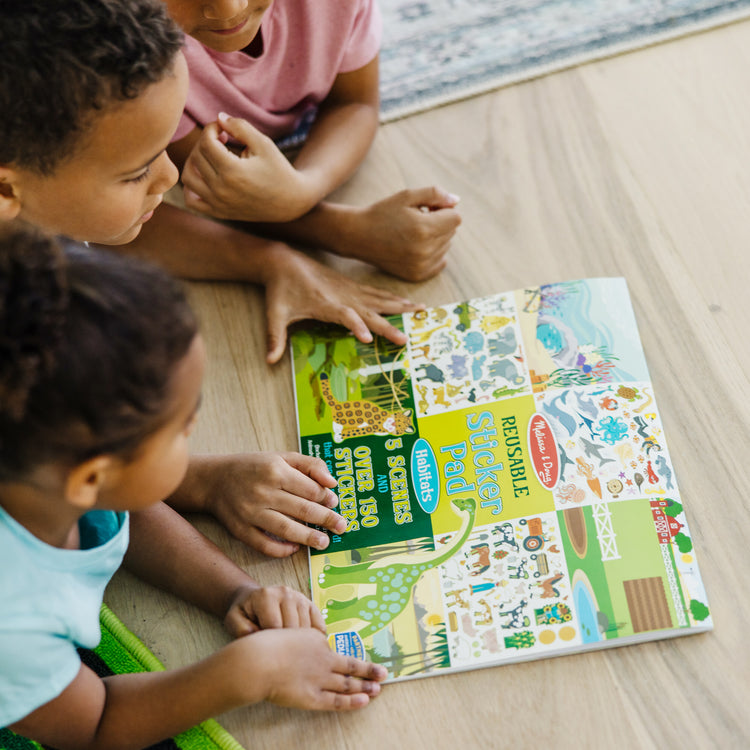 A kid playing with The Melissa & Doug Reusable Sticker Pad: Habitats - 150+ Reusable Stickers