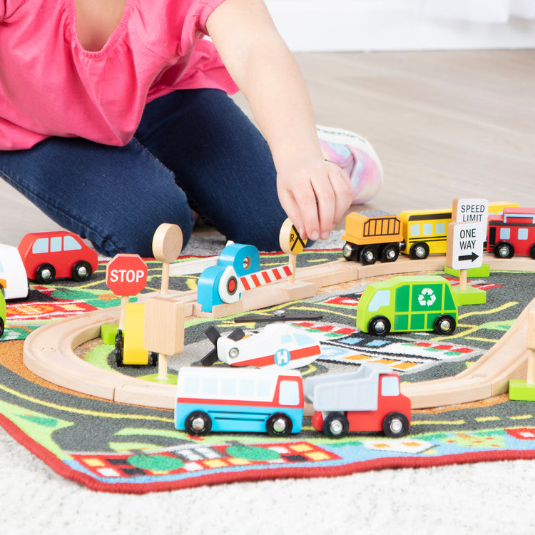 A kid playing with The Melissa & Doug Deluxe Multi-Vehicle Activity Rug (39.5" x 36.5") - 19 Vehicles, 12 Wooden Signs, Train Tracks