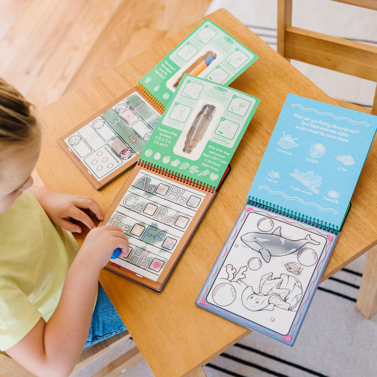 A kid playing with The Melissa & Doug Water Wow! - Water Reveal Pad Bundle - Animals, Alphabet, Numbers and More