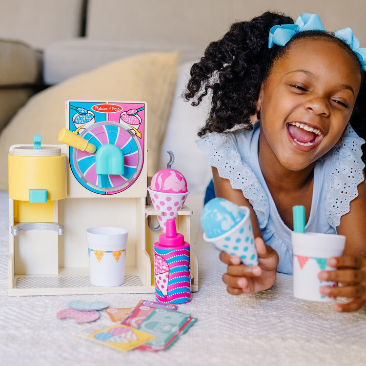 A kid playing with The Melissa & Doug Fun at the Fair! Wooden Snow-Cone and Slushie Play Food Set