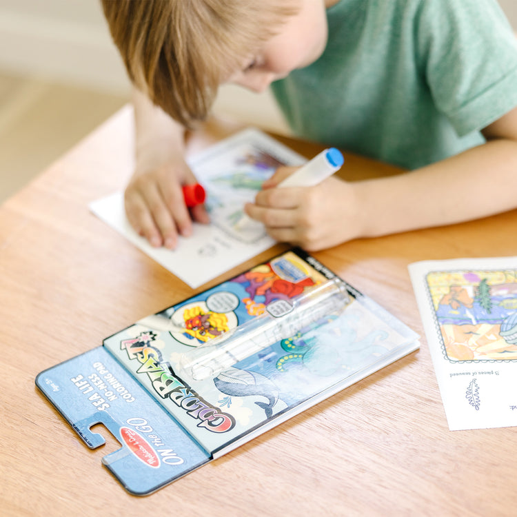 A kid playing with The Melissa & Doug On the Go ColorBlast! Activity Book: Sea Life - 24 Pictures and No-Mess Pen