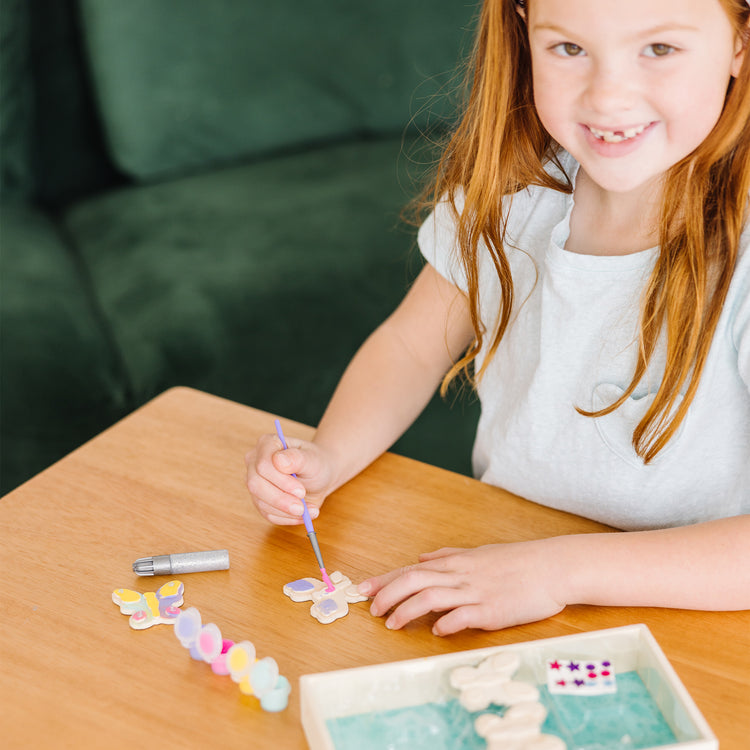 A kid playing with The Melissa & Doug Created by Me! Wooden Butterfly Magnets Craft Kit (4 Designs, 4 Paints, Stickers, Glitter Glue)