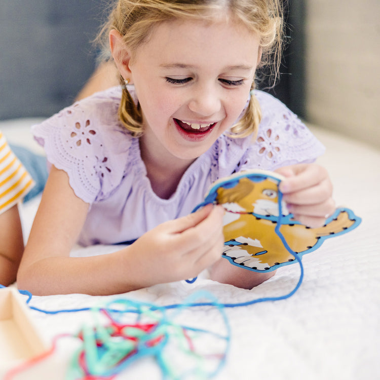 A kid playing with The Melissa & Doug Lace and Trace Activity Set: Pets - 5 Wooden Panels and 5 Matching Laces