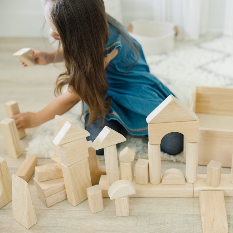 A kid playing with The Melissa & Doug Standard Unit Solid-Wood Building Blocks With Wooden Storage Tray (60 pcs)