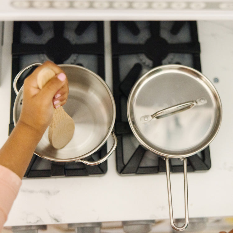 A kid playing with The Melissa & Doug Stainless Steel Pots and Pans Pretend Play Kitchen Set for Kids (8 pcs)